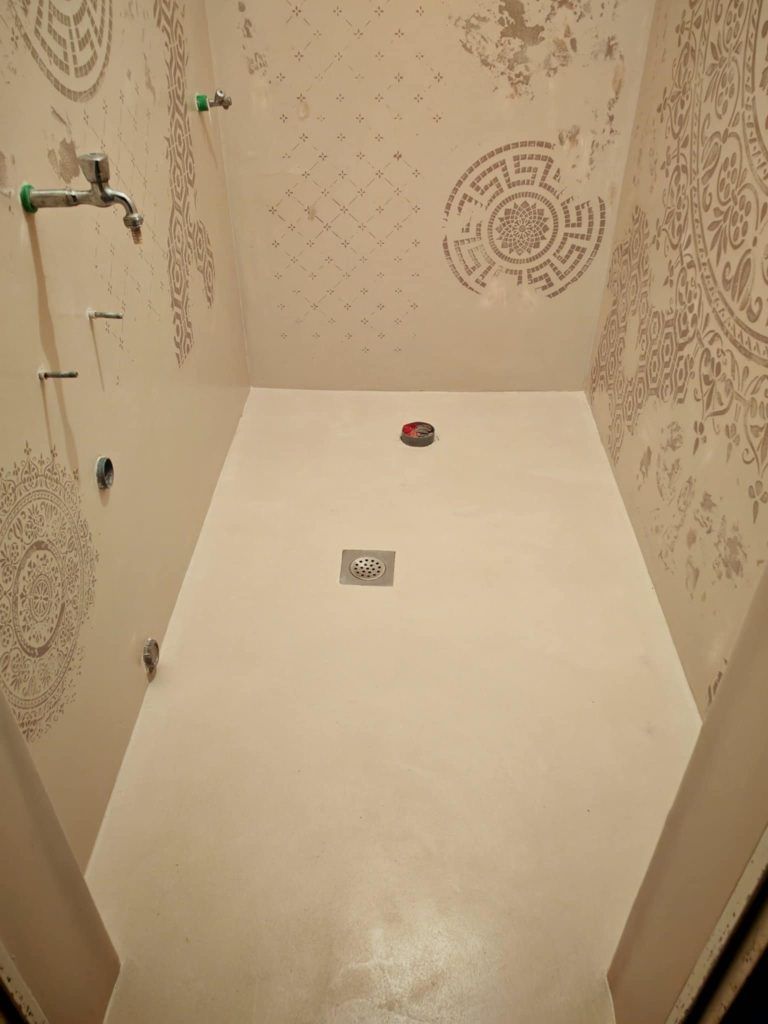 Modern shower area finished with glossy microcement floor and decorative stencil patterns on the walls.