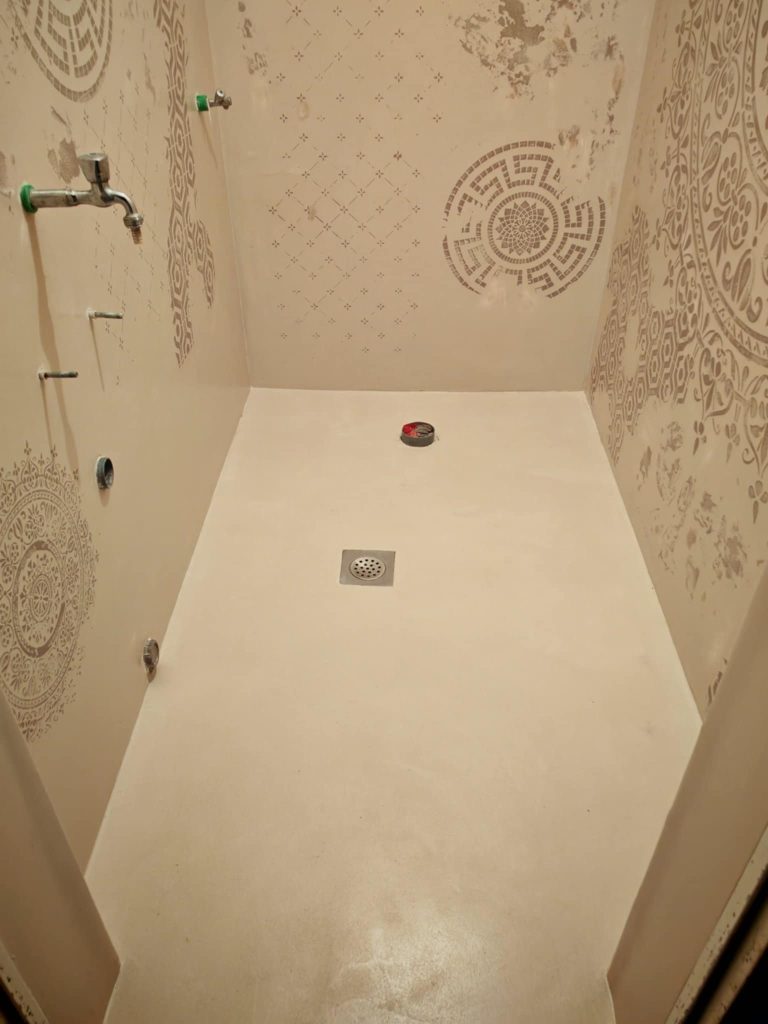 Modern shower area finished with glossy microcement floor and decorative stencil patterns on the walls.