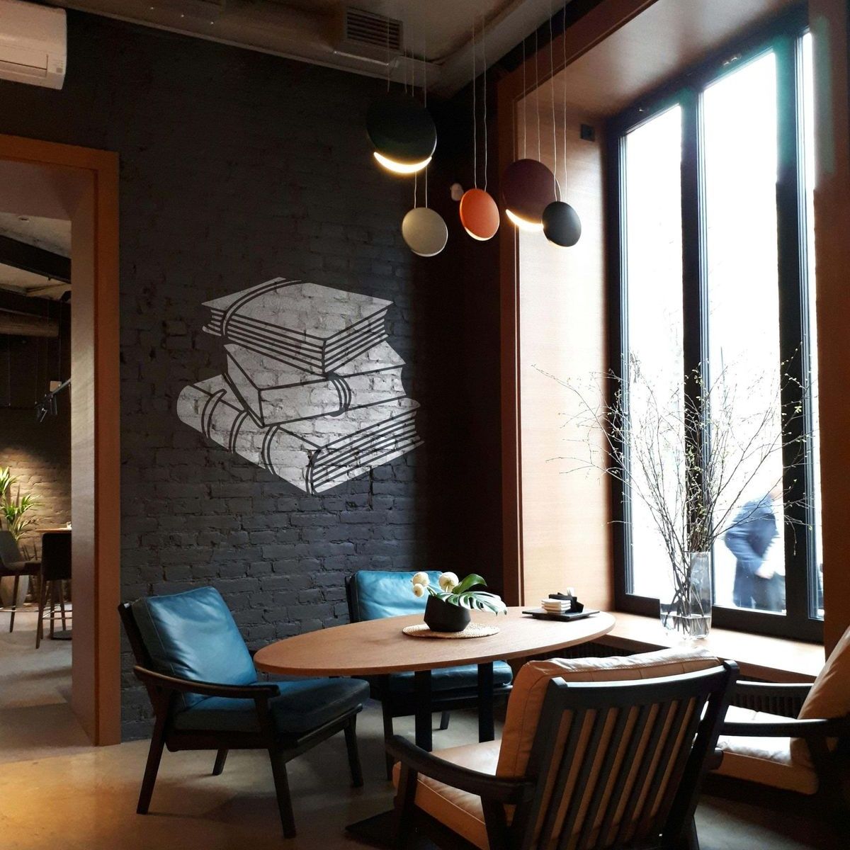 White Books Stencil featuring stacked books on a black brick wall in an industrial-style café with blue chairs.