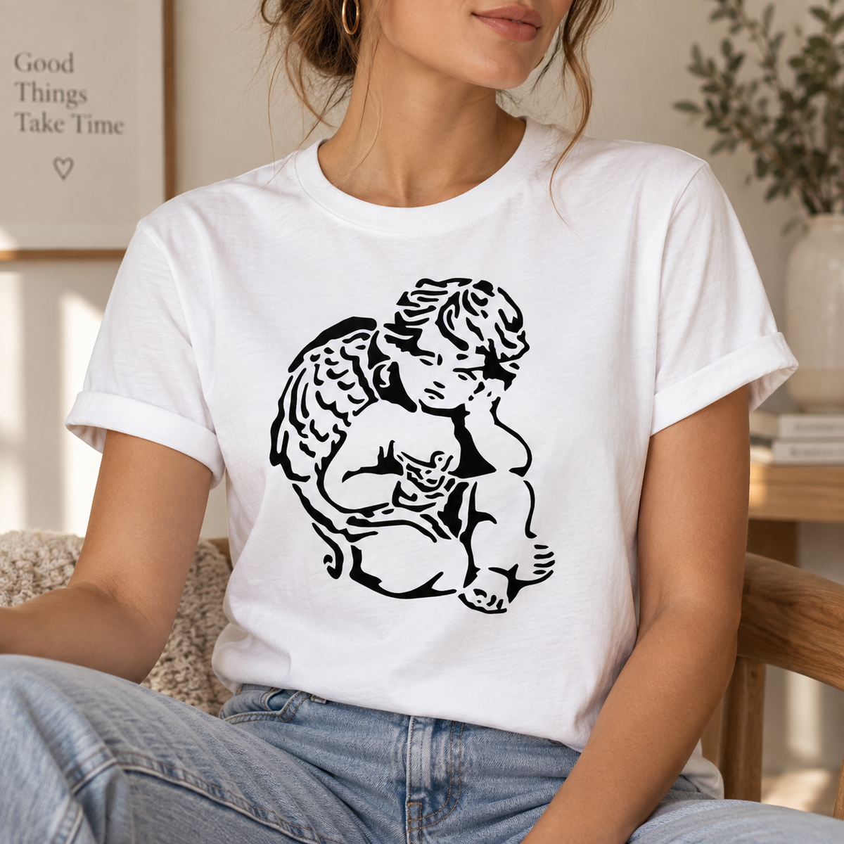 Black cherub angel stencil printed on a white T-shirt in a warm neutral lifestyle setting.