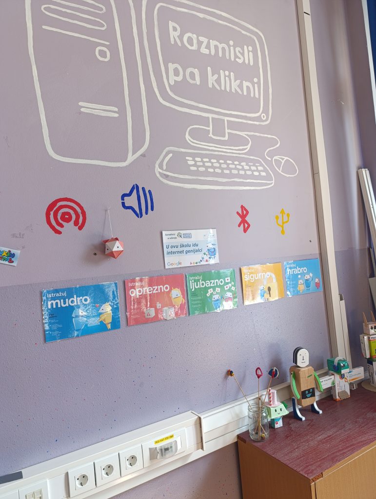 Classroom wall decorated with a large computer illustration and the message “Razmisli pa klikni,” surrounded by colorful internet safety posters and painted technology icons.