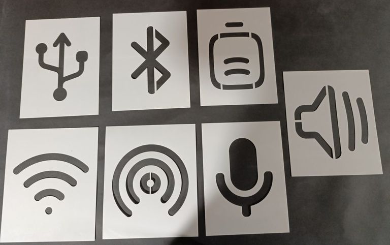 Set of technology symbol stencils featuring USB, Bluetooth, smartphone, speaker, Wi-Fi, signal, and microphone icons arranged on a dark surface.