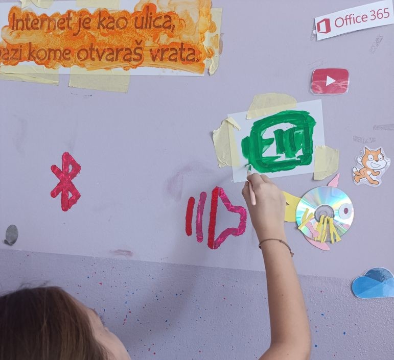 Student painting a green icon on a classroom wall using a stencil, carefully filling in the design during a creative activity.