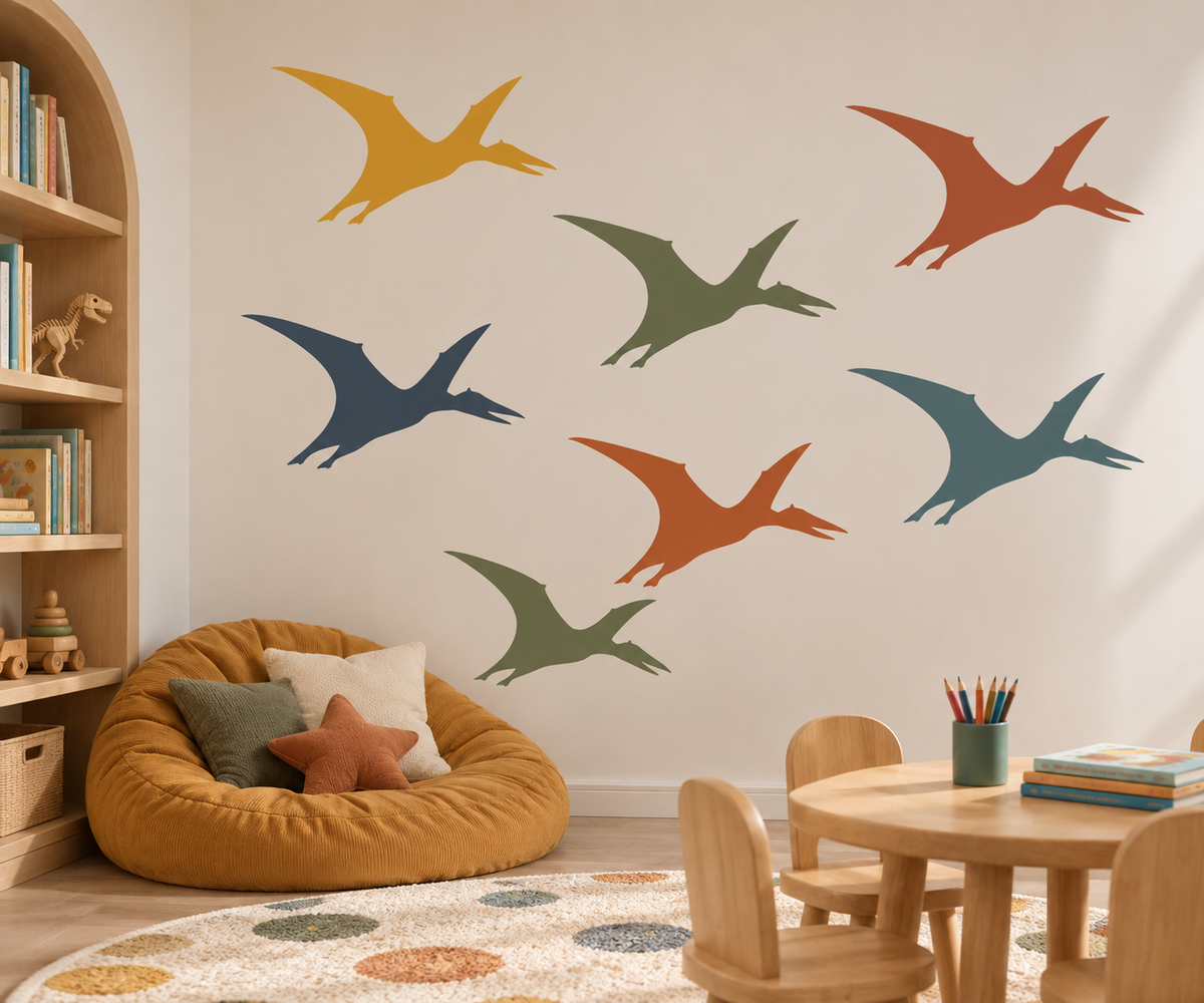 Colorful pterosaur stencils painted on a white wall in a cozy children’s playroom with wooden furniture and a reading corner.