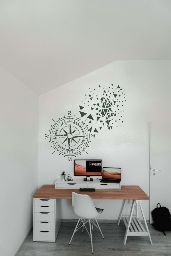 Modern home office wall decorated with a large compass stencil and abstract geometric pattern above a minimalist desk setup.