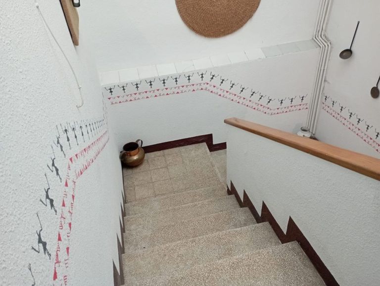 Staircase descending with a decorative stencil border of tribal-style figures and geometric accents following the angle of the steps along the wall.