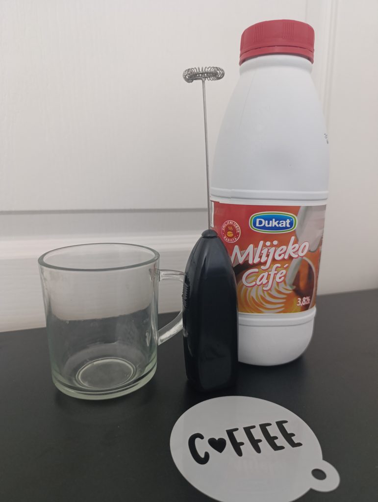 Frothing milk for coffee stencil art, showing barista-style foam being poured over a stencil to create a decorative design on the drink’s surface.