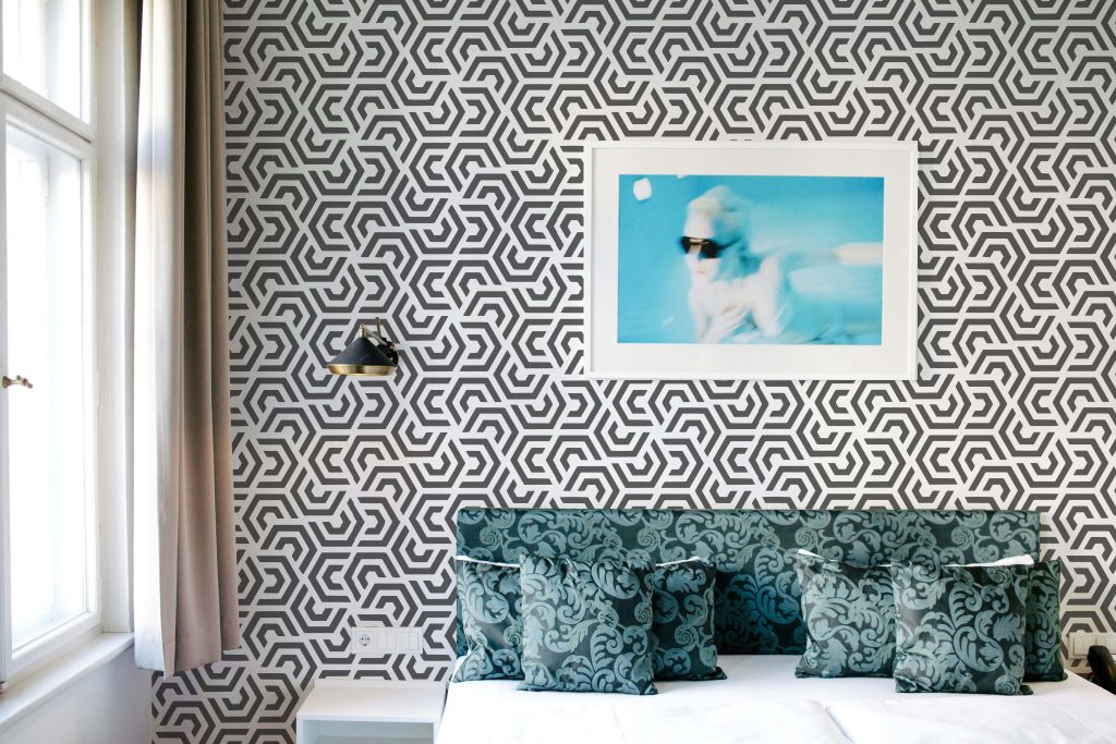 Bedroom accent wall featuring a bold geometric hexagon stencil pattern in black and white behind a bed with patterned cushions.