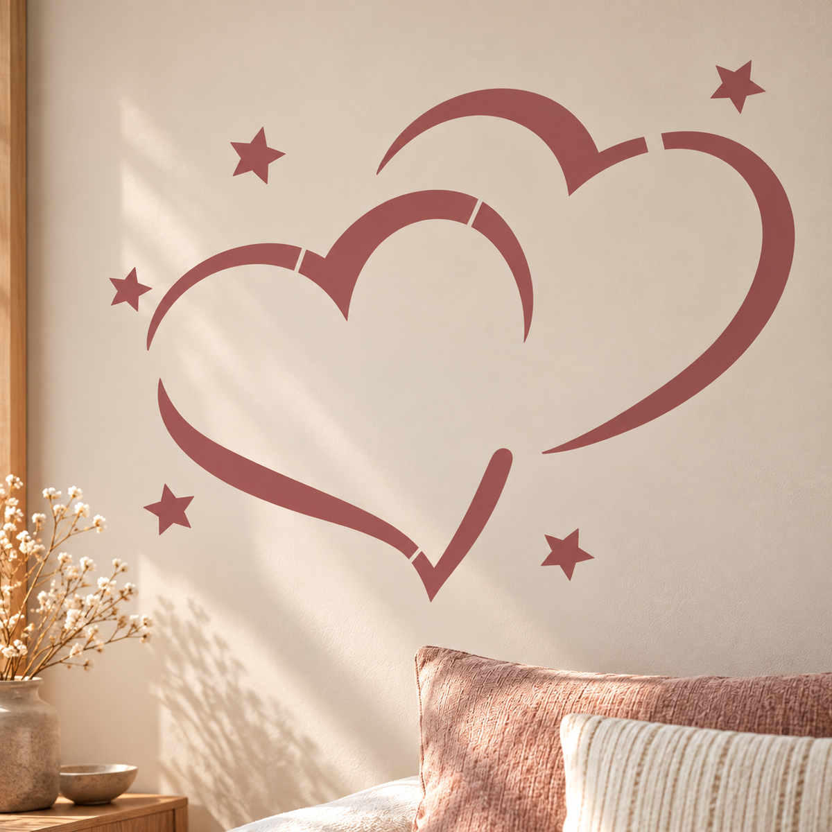 Hearts and Stars Stencil in dusty rose on a cream wall above a bed with soft pink cushions.