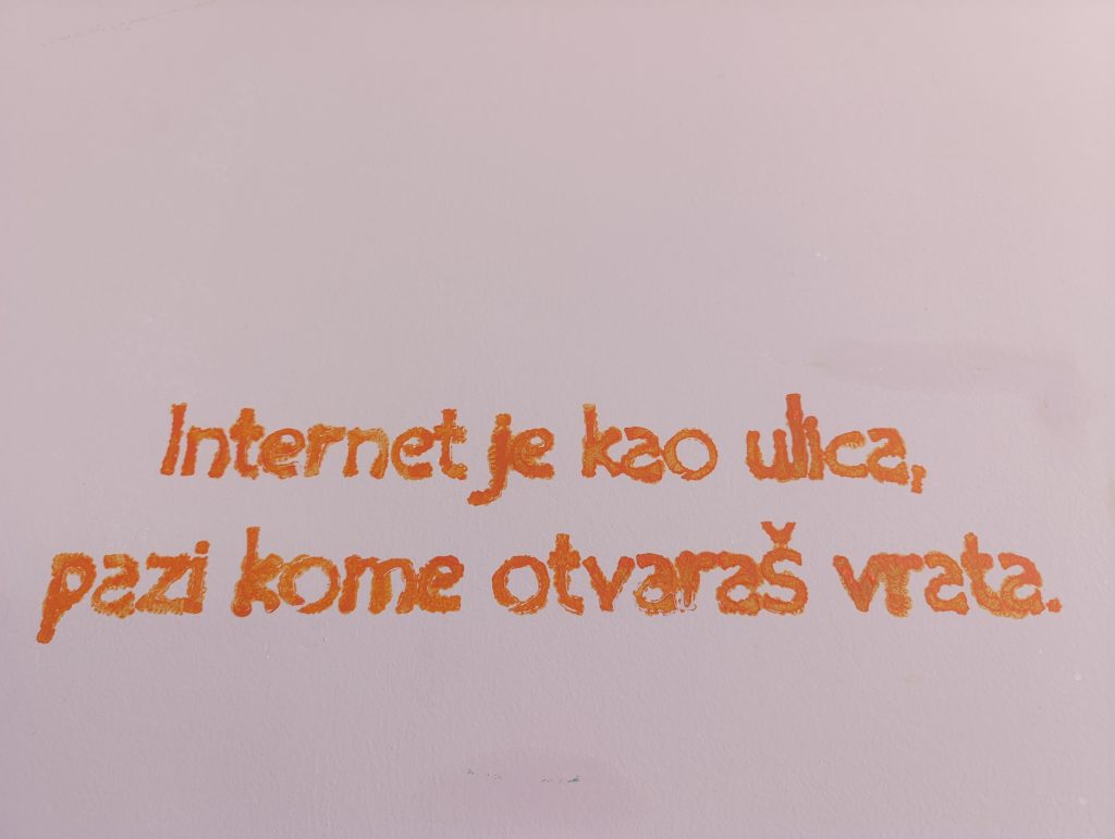 Orange painted wall quote reading “Internet je kao ulica, pazi kome otvaraš vrata.” promoting online safety awareness.