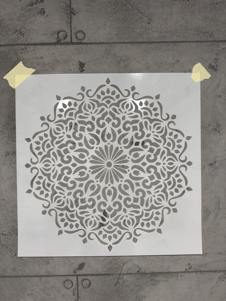 Intricate circular mandala stencil taped to a concrete wall, ready for decorative painting application.