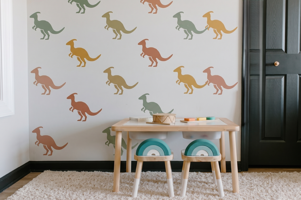 Pastel Parasaurolophus dinosaur stencil pattern in sage green, terracotta, mustard, and dusty blue on a neutral kids playroom wall with wooden furniture and soft decor.