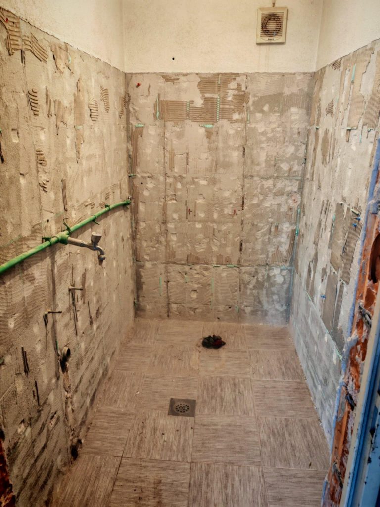 Bathroom interior with tiles and fixtures removed, showing bare walls and plumbing during renovation.