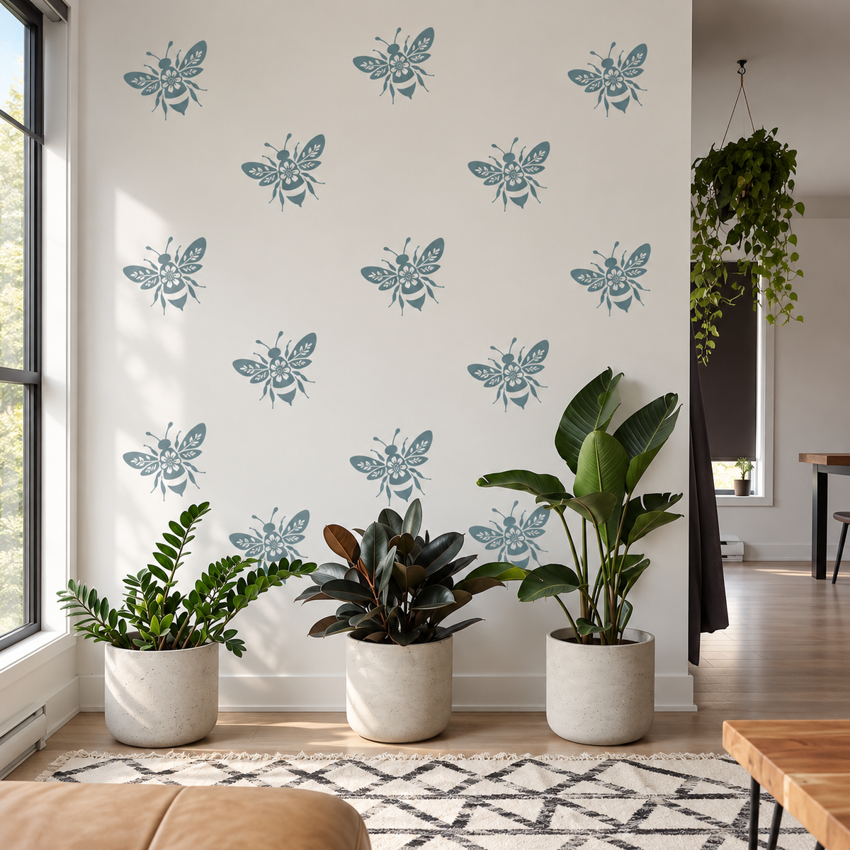Reusable floral bee stencil repeated in dusty blue on a bright white wall, styled with lush indoor plants in a modern sunlit room.reusable-bee-stencil-neut