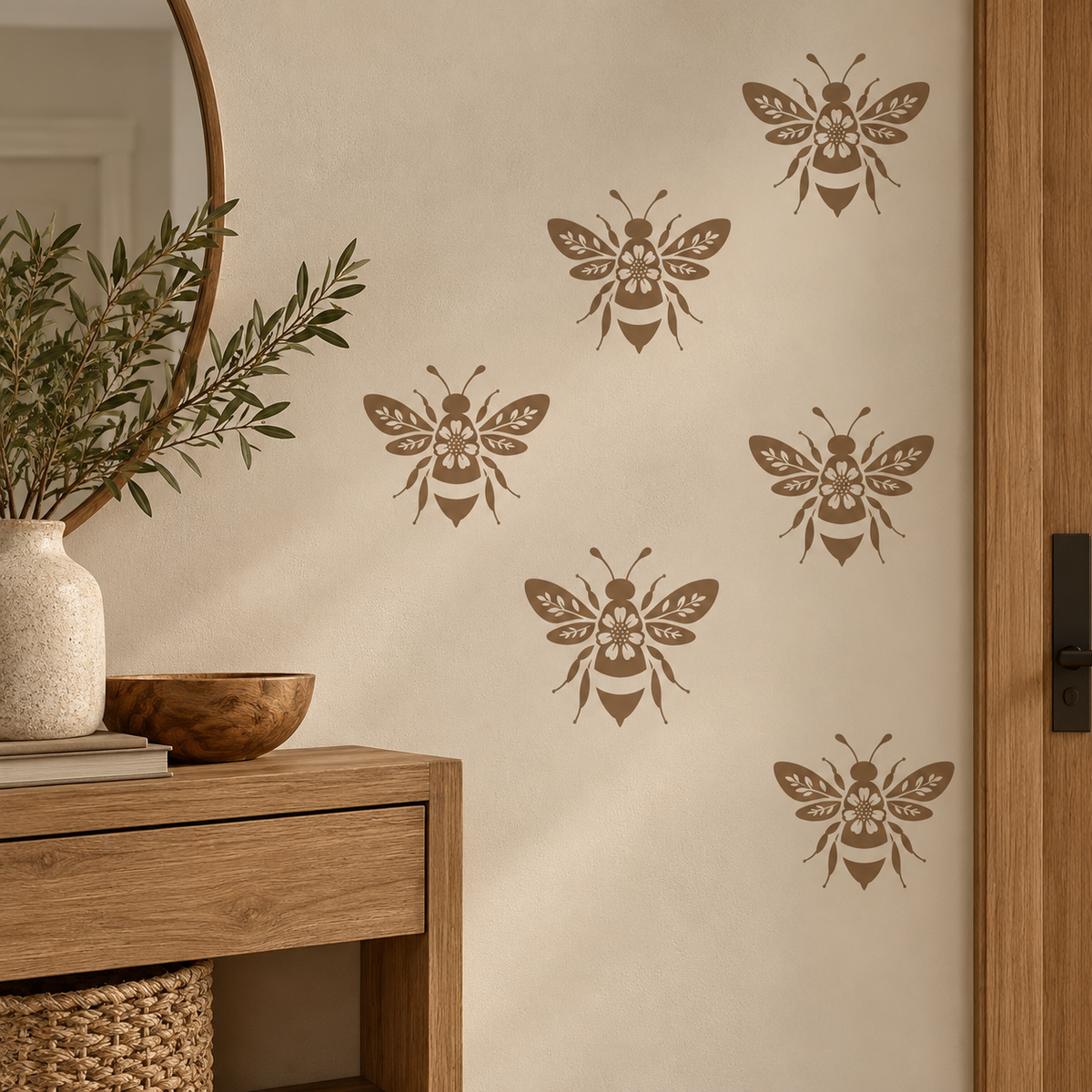Reusable bee stencil in warm taupe arranged across a cream entryway wall with natural wood furniture and organic decor.