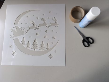 Santa sleigh stencil with crafting supplies arranged on a table, ready for creating a festive holiday decoration.