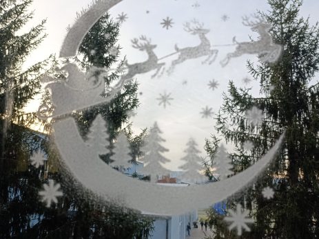 Santa sleigh stencil with reindeer and Christmas trees sprayed with artificial snow on a window