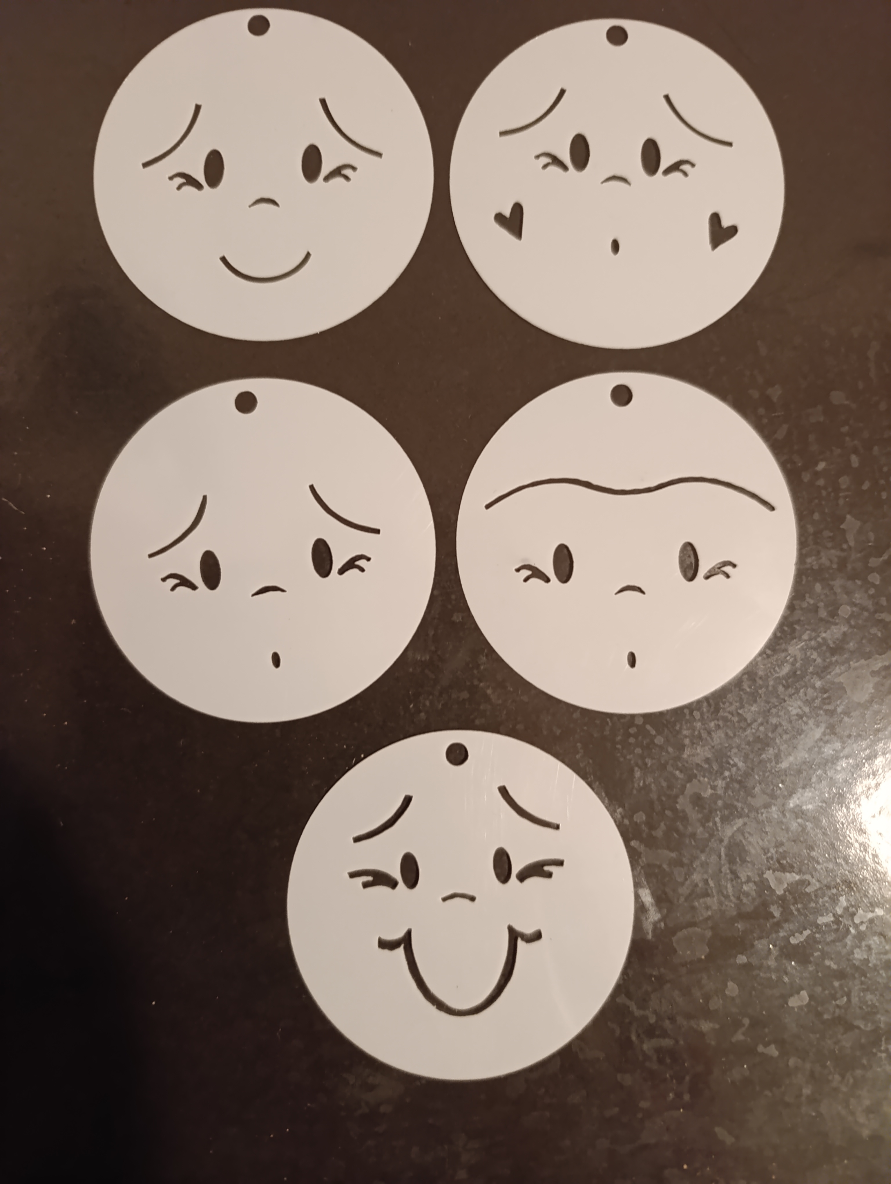 Collection of five white circular face stencils with different cute facial expressions displayed on a dark surface.