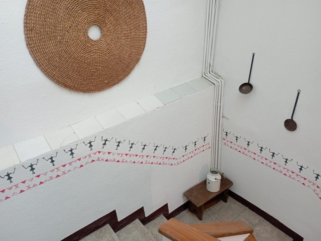 Overhead view of a stairwell decorated with a repeating stencil border pattern of black human silhouettes and red geometric shapes on textured white walls.