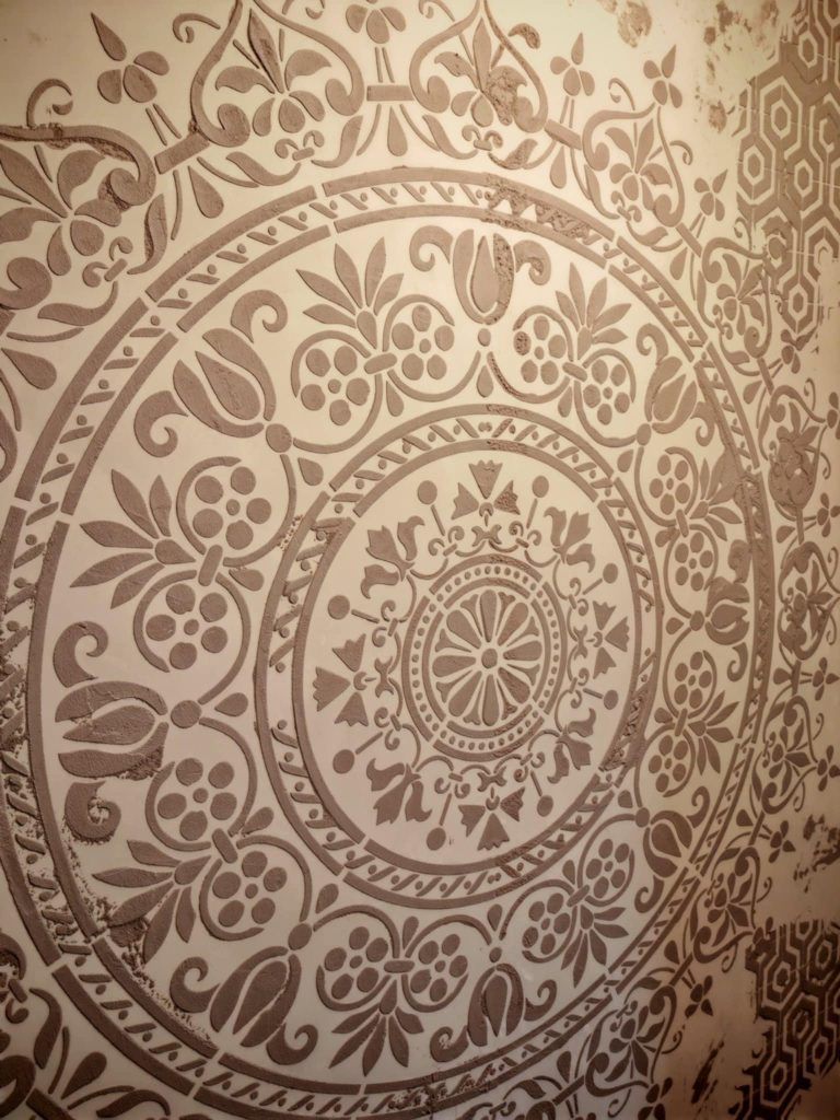 Close-up of an ornate mandala stencil pattern applied on a textured microcement wall during renovation.