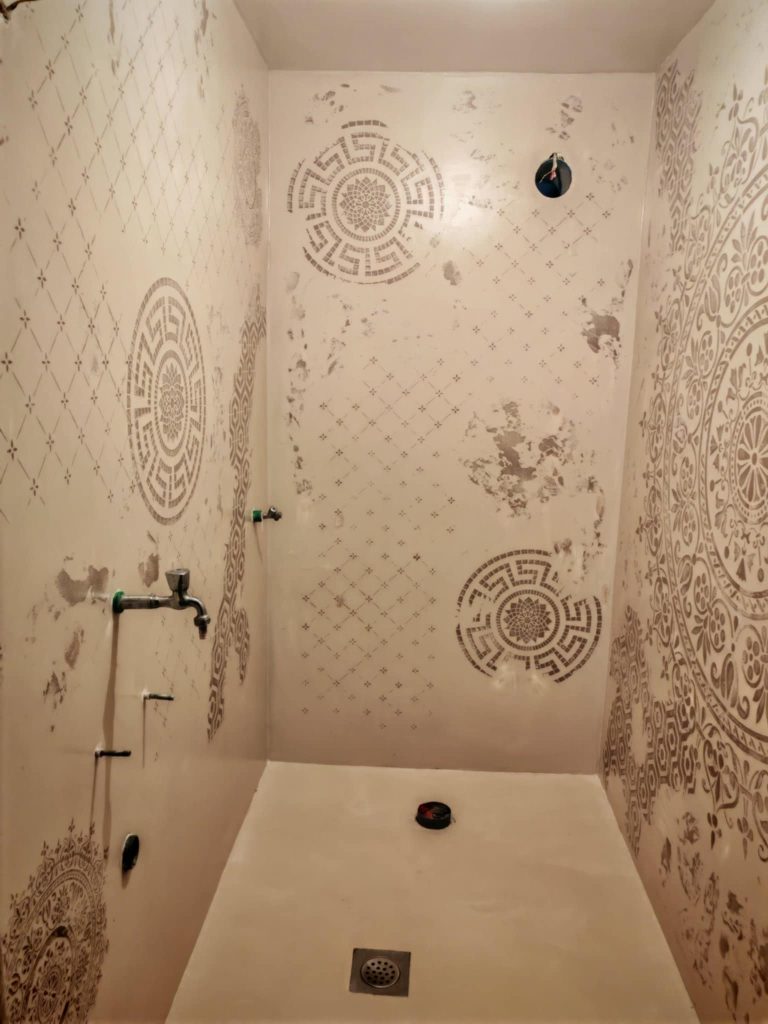 Walk-in shower with decorative mandala and geometric stencil patterns applied to the walls, creating a textured, artistic finish.