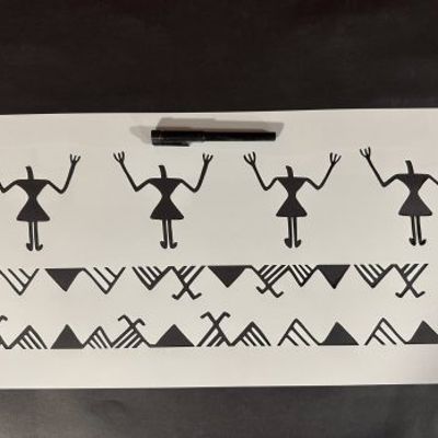 Stencil sheet featuring repeating tribal-style human figures and geometric border patterns placed on a table with a pen above it.