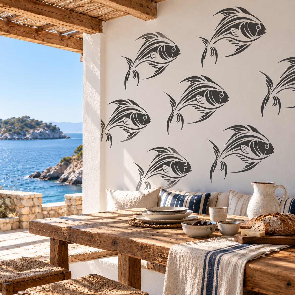 Dark gray tropical fish stencils decorating a cream terrace wall beside a rustic dining table overlooking the blue sea. 