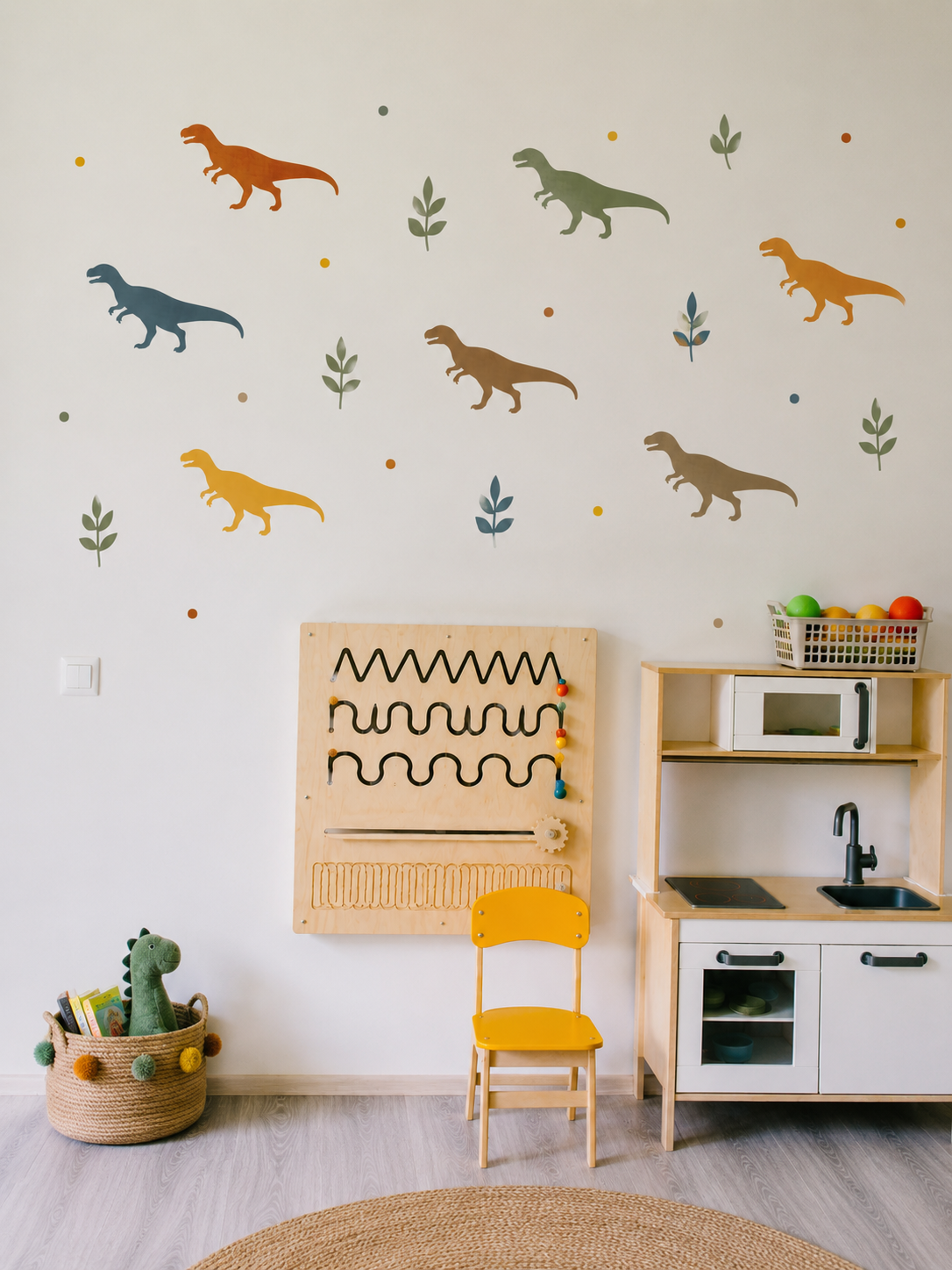 Colorful Tyrannosaurus Rex dinosaur stencil decals with leaf accents on a neutral nursery wall above a Montessori-inspired play kitchen and wooden activity board in a modern kids playroom.