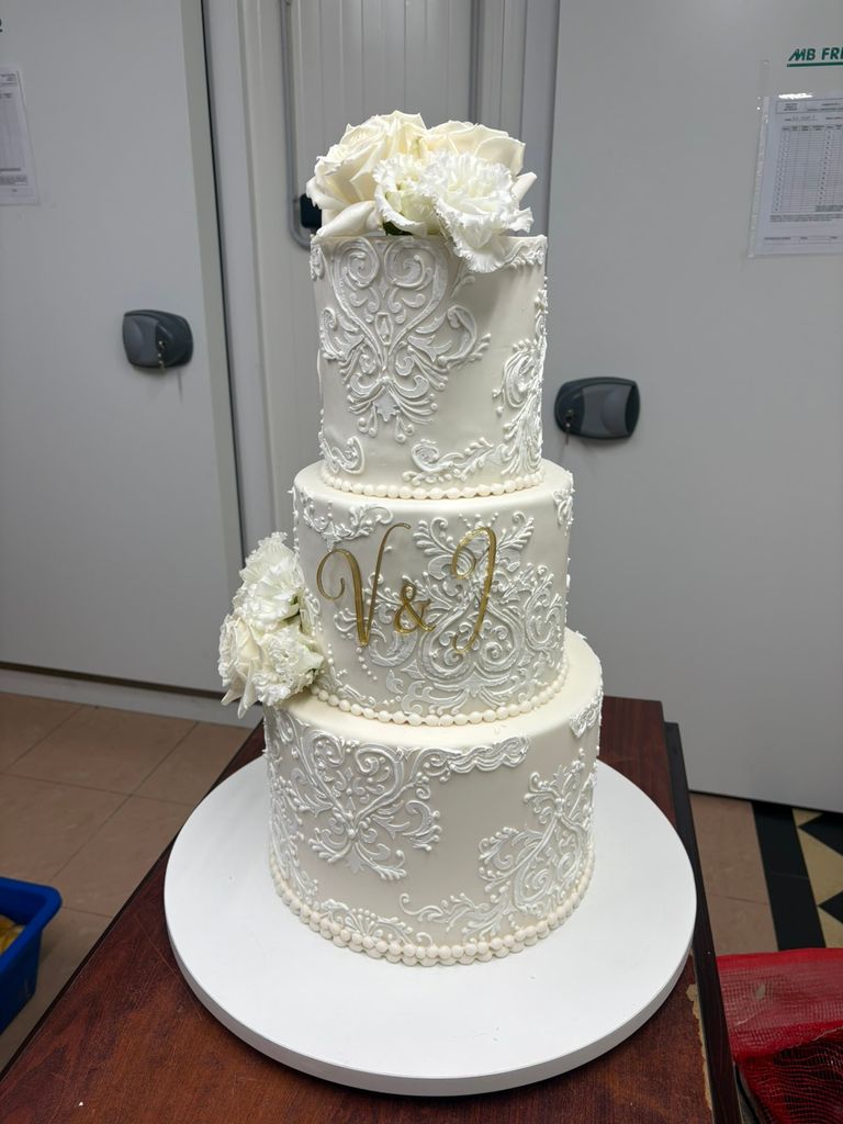 Elegant white wedding cake decorated with intricate cake stencil patterns, gold initials and white flowers